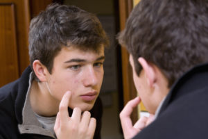teenage boy looking at the mirror as he's picking at his face