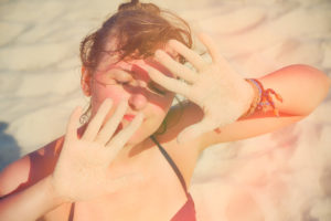 A woman with a skin allergy holding her hands up to the sun to cover her face.