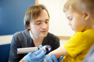 A caring pediatric dermatologist checks moles on the skin of a small child.
