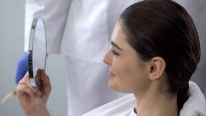 Female looking in mirror after cosmetic procedure, and smiles with satisfaction.